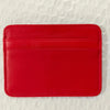 Leuchtend rotes echtes Kuhfell-Kartenschlüsselhalter-Wallet auf weißer strukturierter Oberfläche