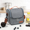 A gray insulated reusable lunch bag with an orange strap is shown on a white surface.