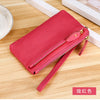 A vibrant red genuine leather wristlet clutch wallet with a zipper closure resting on a wooden surface.