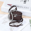 A dark brown leather coin purse with a silver chain and lanyard is displayed on a white background next to a book.