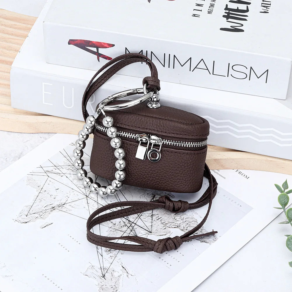 A dark brown leather coin purse with a silver chain and lanyard is displayed on a white background next to a book.