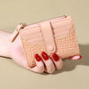 A hand holds a light pink PU leather card wallet with a quilted pattern and double zip closure.