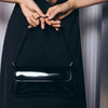 A person holds a black PU leather shoulder bag with an adjustable strap against a dark background.