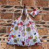 A white Miffy folding shopping bag featuring colorful illustrations of Miffy and flowers, displayed against a brick wall.