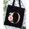 Black canvas tote bag featuring a rose floral design in rose gold on the side.