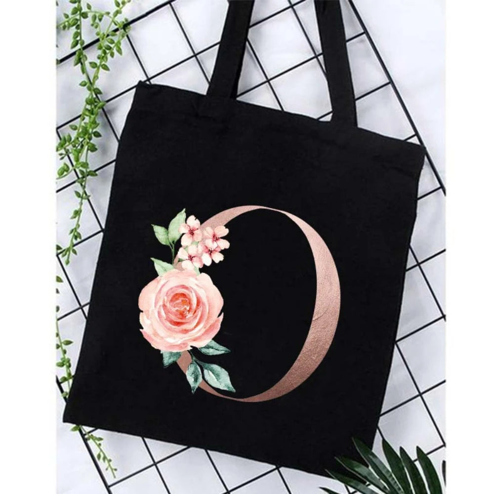 Black canvas tote bag featuring a rose floral design in rose gold on the side.