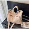 Un sac à épaule en velours rayé côtelé beige clair est exposé sur une surface sombre.