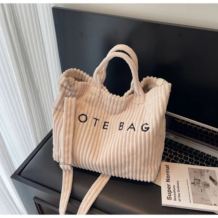 Un sac à épaule en velours rayé côtelé beige clair est exposé sur une surface sombre.
