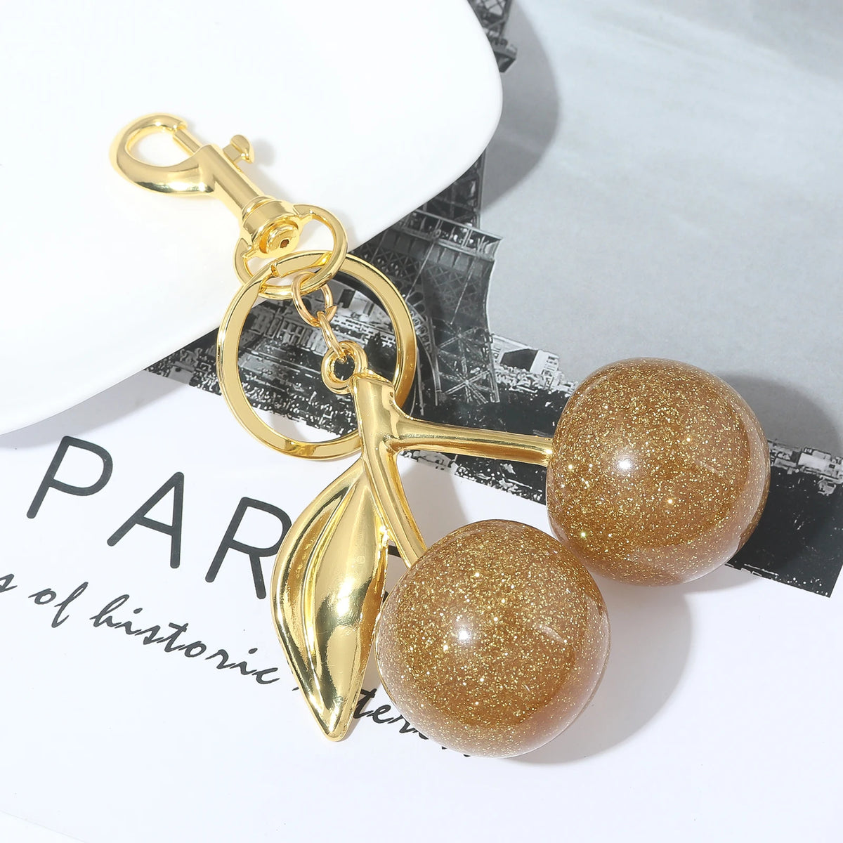 Gold-toned keychain featuring a pink crystal cherry fruit charm on a gold chain.