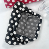 A black and white polka dot clutch bag is shown next to a clear glass.