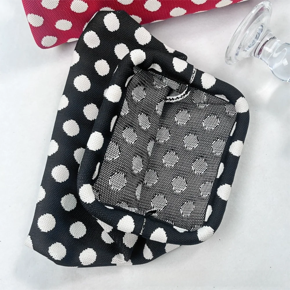 A black and white polka dot clutch bag is shown next to a clear glass.