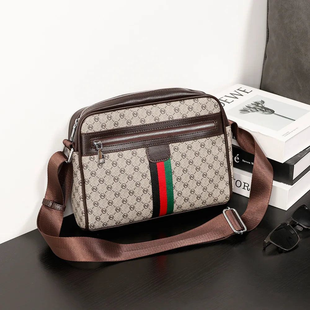A brown men's letter print crossbody sling bag resting on a dark surface next to a stack of books.