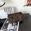 A brown leopard print makeup organizer bag resting on a dark surface next to a magazine.