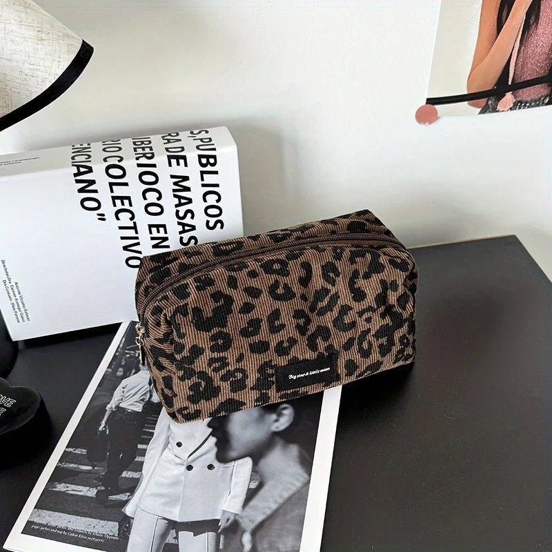 A brown leopard print makeup organizer bag resting on a dark surface next to a magazine.