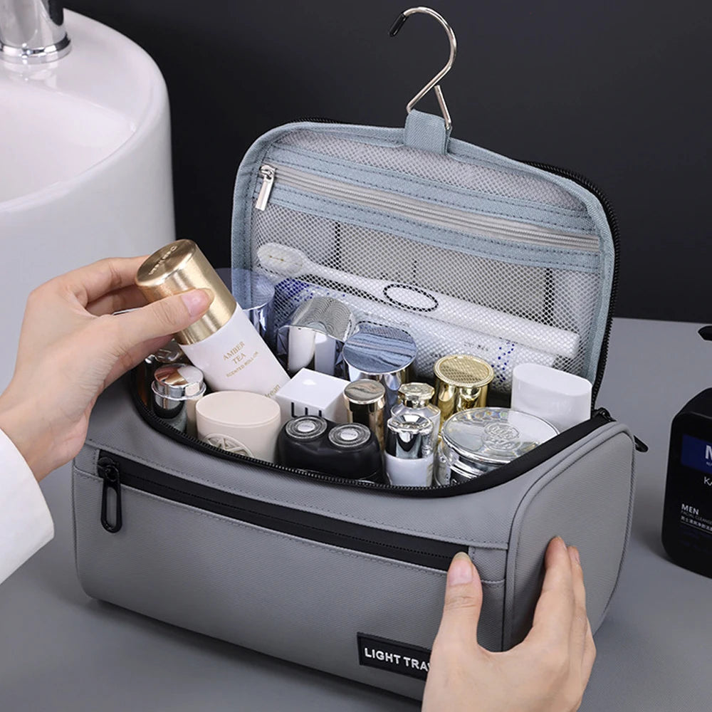 A hand is opening a light gray travel toiletry bag filled with various grooming products and a brush.