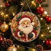 A Christmas tree decorated with a circular painting featuring Santa Claus and holly, surrounded by ornaments and pine cones.