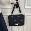 Bolso para portátil acolchado negro con detalles de lazo azul colgado en un marco de puerta blanca.
