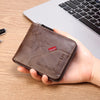 A brown leather bifold wallet with a silver clasp and embossed initials is held over a wooden desk next to a laptop.