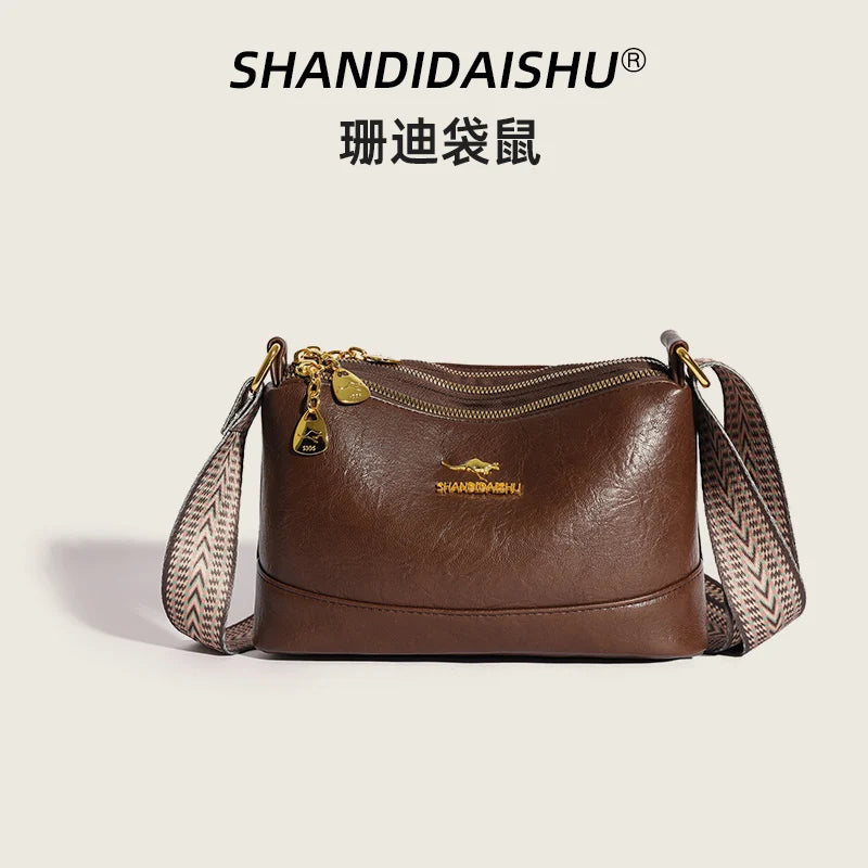 A brown luxury PU leather crossbody handbag with gold hardware and a patterned strap.
