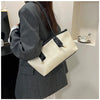A woman holds a beige classic PU leather tote bag with black hardware against a light wall.