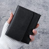 A hand holds a black slim multi-functional card wallet against a gray background.