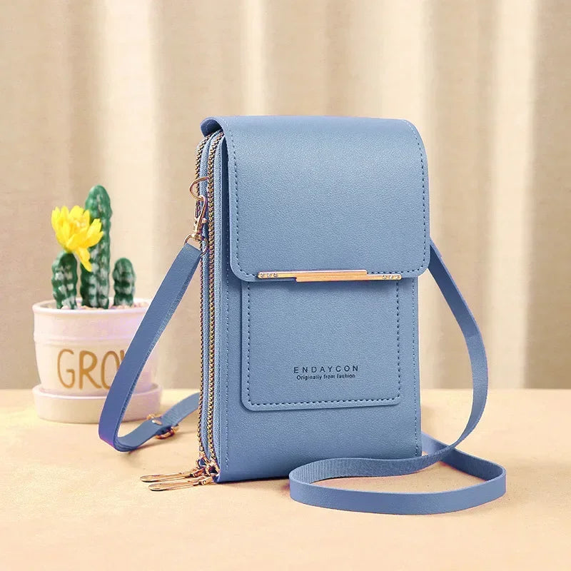 A light blue women's touch screen crossbody shoulder bag with gold hardware resting on a beige surface.