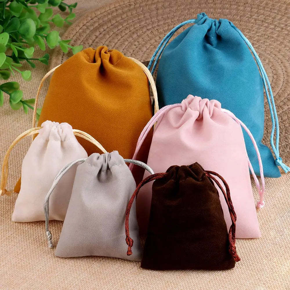 Un juego de cinco bolsas de regalo de terciopelo suave con cordón en tonos naranja, azul, rosa, beige y marrón, sobre una sup
