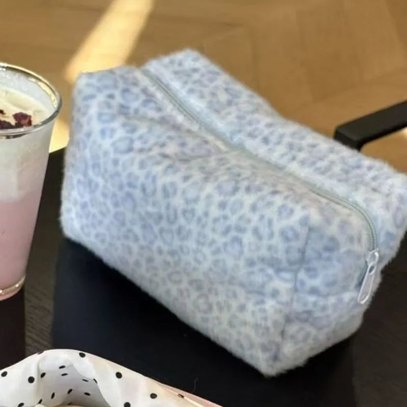Bolsa de maquillaje para viajar con estampado de leopardo azul claro sobre una superficie oscura junto a un vaso.