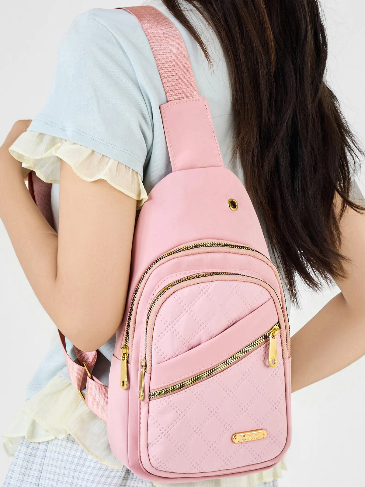 Un sac bandoulière matelassé rose avec une sangle rose porté par une personne en haut bleu clair.