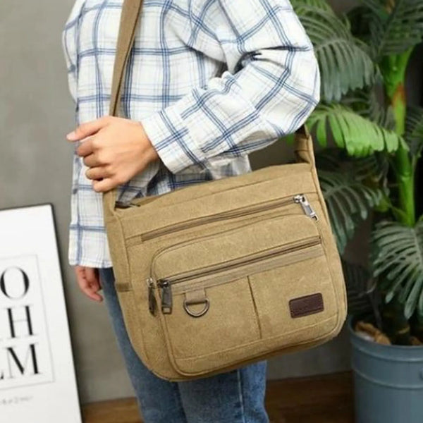 A person is holding a tan canvas tool bag with multiple pockets against a blurred green background.
