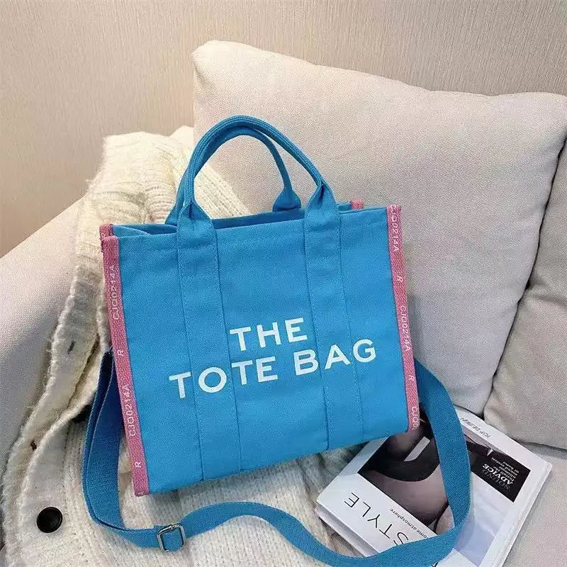A bright blue tote bag with pink trim is displayed on a white surface next to a light-colored blanket.