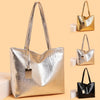 A silver metallic zipper tote bag displayed against a beige background with other gold and black versions.