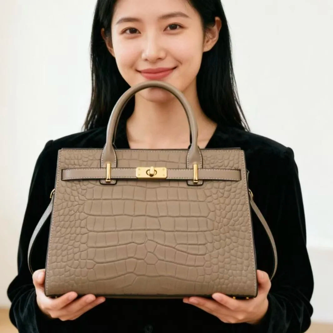 A woman holds a beige genuine leather shoulder bag with gold hardware against a white background.