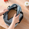 A hand is holding an insulated lunch tote bag with a waterproof lining on a wooden table.