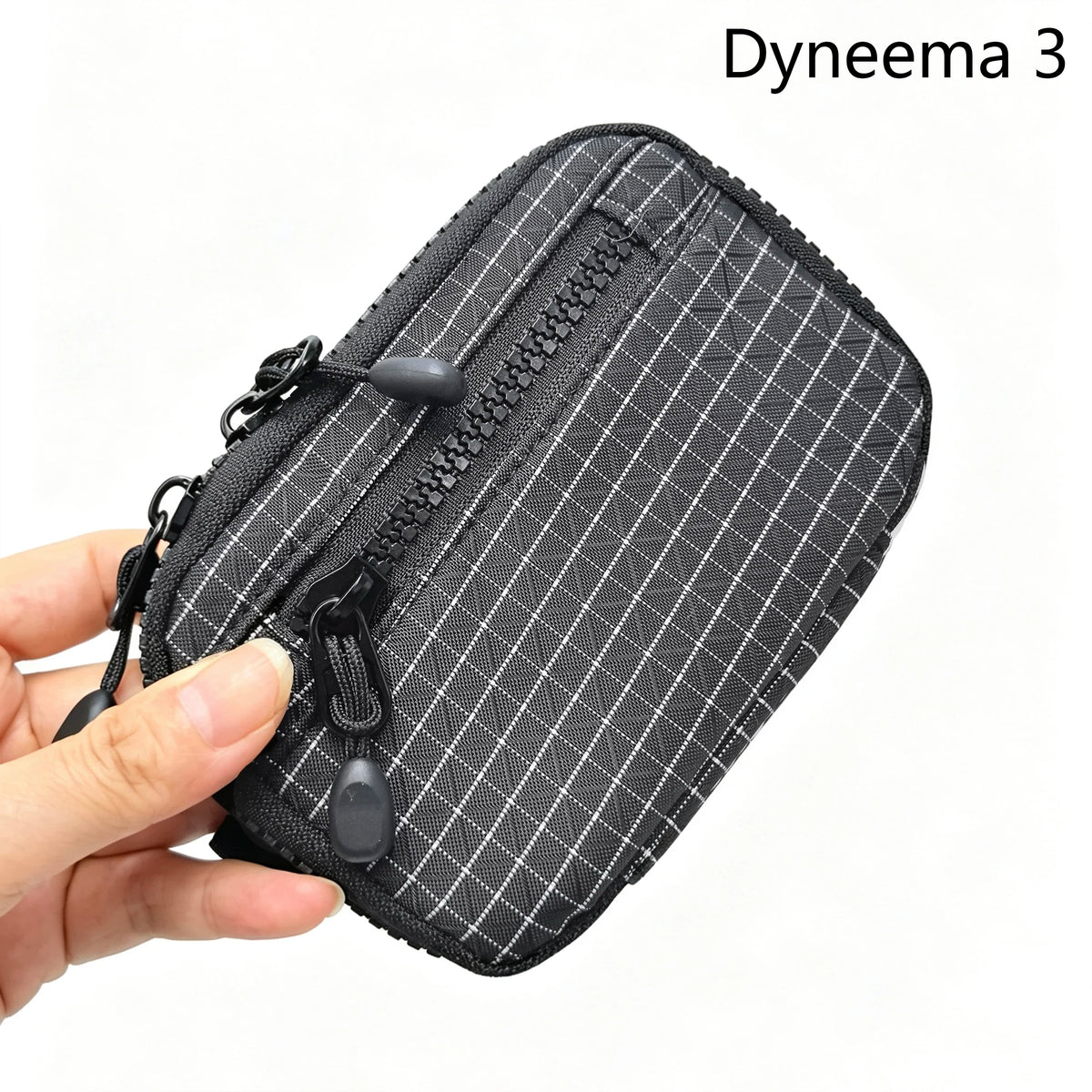 Une pochette utilitaire noire en Dyneema 3 à motif grille diamant tenue par une main.
