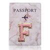 Una funda de pasaporte de imitación de cuero rosa claro con una inicial F dorada y un ícono de avión negro.