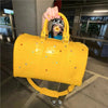 A bright yellow faux crocodile tote bag with crystal accents is held by a person indoors.