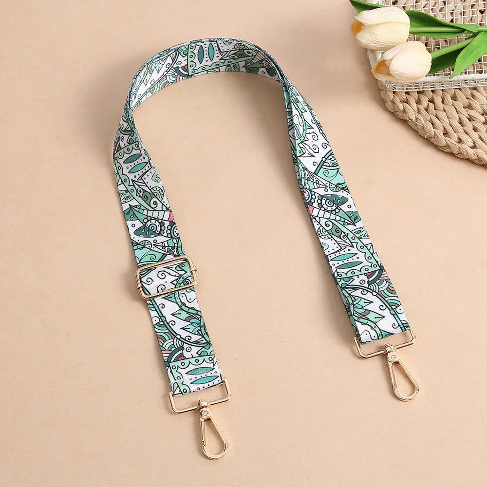 A beige adjustable bohemian printed crossbody strap with a white and green pattern is displayed against a neutral background.
