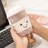 A hand holds a beige cartoon character plush decor shaped like a cylinder with a smiling face.