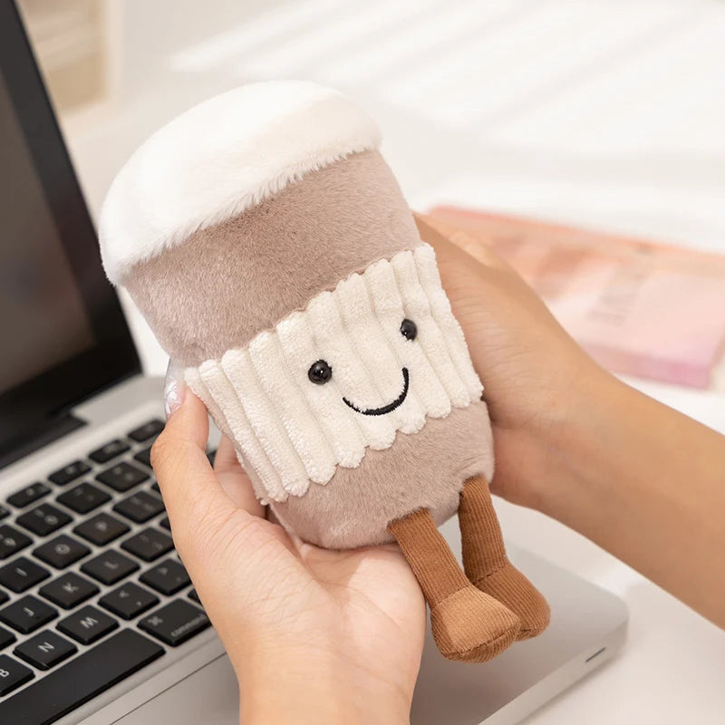 A hand holds a beige cartoon character plush decor shaped like a cylinder with a smiling face.