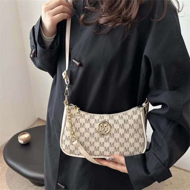 Una mujer sostiene un bolso cruz de mano vintage dorado con monograma blanco y gris.