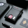 A black slim minimalist men's wallet with RFID protection, a smartwatch, and a pen resting on a dark surface.