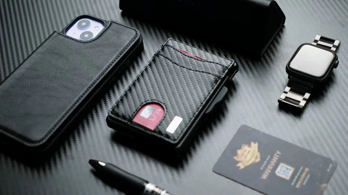 A black slim minimalist men's wallet with RFID protection, a smartwatch, and a pen resting on a dark surface.