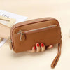 A brown genuine cowhide leather double-zip wristlet wallet is held in a hand on a light background.