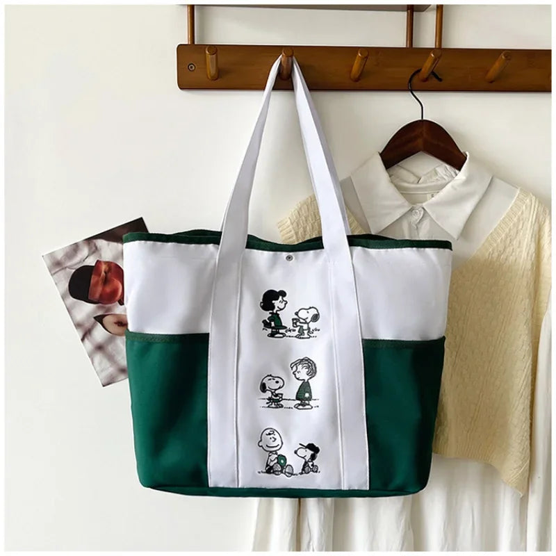 A green and white canvas tote bag featuring Snoopy characters, hanging on a wooden rack.