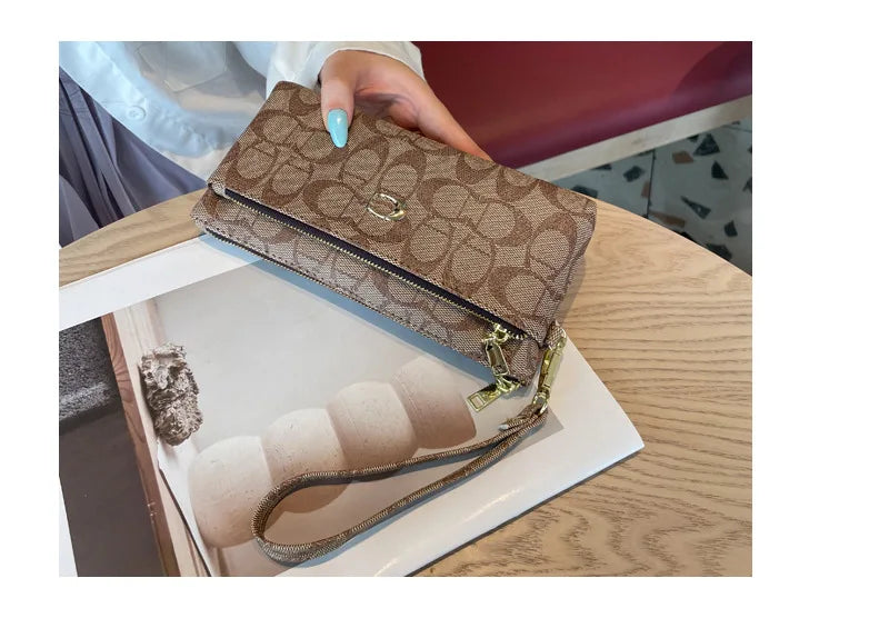 A brown patterned zipper wallet is shown being held by a hand, with cards and a leather strap visible.