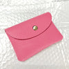 A pink genuine leather card holder and coin purse with a gold-toned clasp resting on a white textured surface.