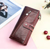 A dark brown genuine leather vintage clutch wallet resting on a pink surface next to a photo and some cherries.