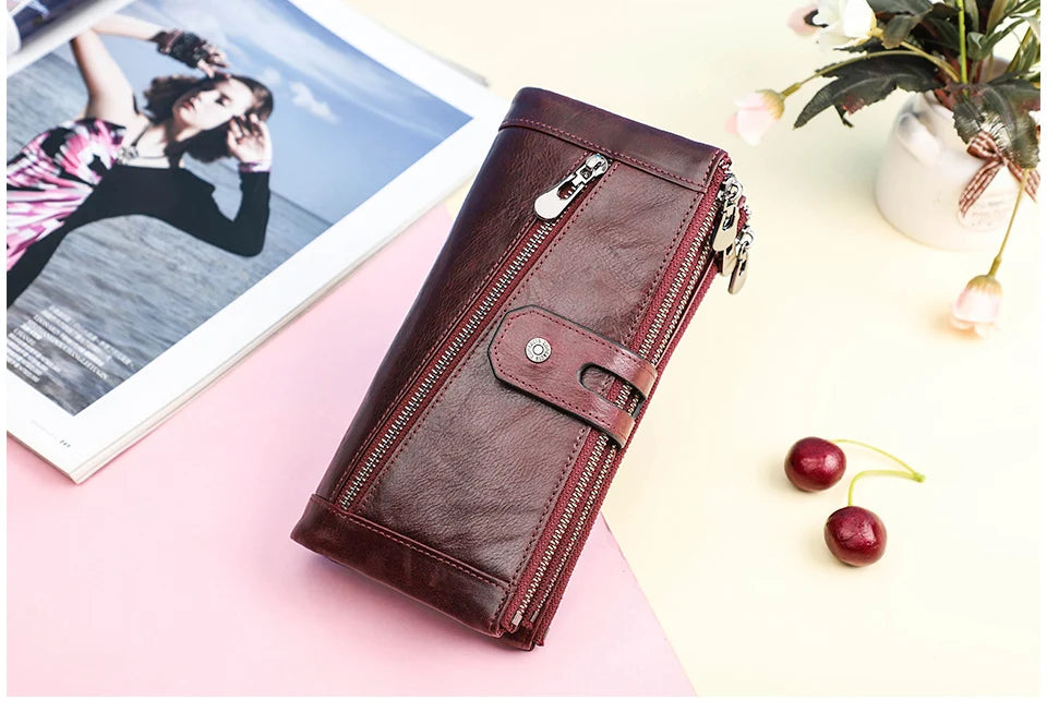 A dark brown genuine leather vintage clutch wallet resting on a pink surface next to a photo and some cherries.