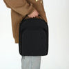 A black unisex travel baseball hat and storage bag being held by a person wearing a brown jacket.